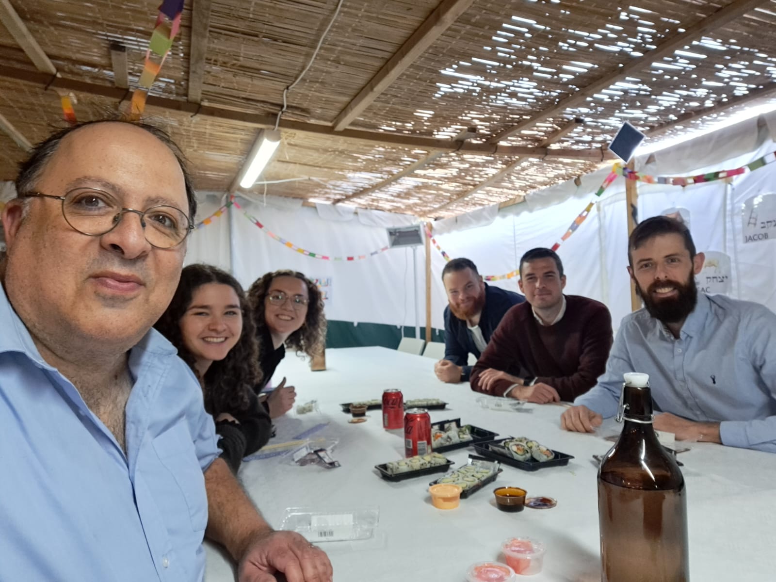 The HIAS+JCORE team sit around a table in a Sukkah.