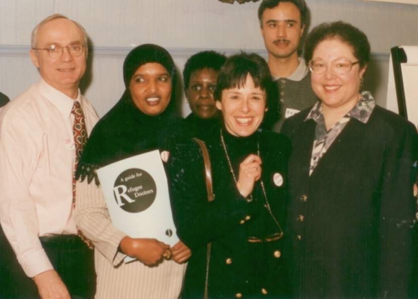 HIAS+JCORE's Honorary President, Dr Edie Friedman, stands smiling with a group of Refugee Doctors, and Dr Richard Stone.